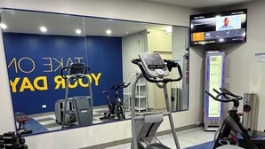 Une salle de sport équipée de matériel d’exercice, d’un banc et d’un écran de télévision affichant un message de bienvenue.