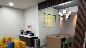 Un salon moderne comprenant un canapé, un coin café, un espace repas avec une table et des chaises, ainsi qu’un élément décoratif mural.