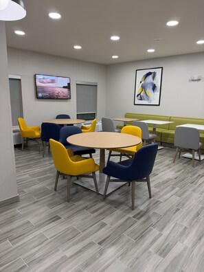 A modern meeting room with a large table, colorful chairs, a sofa, and a TV screen displaying a sunset scene. - Harvey Inn & Suites Harvey - Chicago Southland (Harvey)