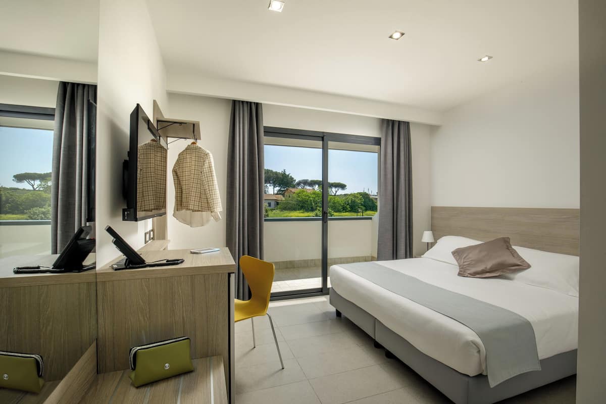 Una habitación de hotel moderna con una cama grande, un escritorio con teléfono, una silla y vistas al exterior.
