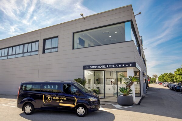A modern hotel building with a parking area and a van labeled "Simon Hotel Apulia." - SIMON HOTEL APRILIA (Aprilia)