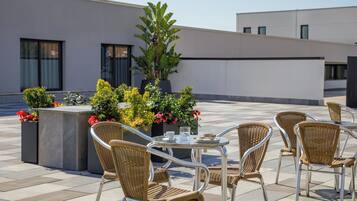 A rooftop terrace with outdoor seating, potted plants, and a view of the building's exterior.