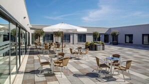 An outdoor patio area with tables and chairs, large umbrellas, and potted plants. - SIMON HOTEL APRILIA (Aprilia)