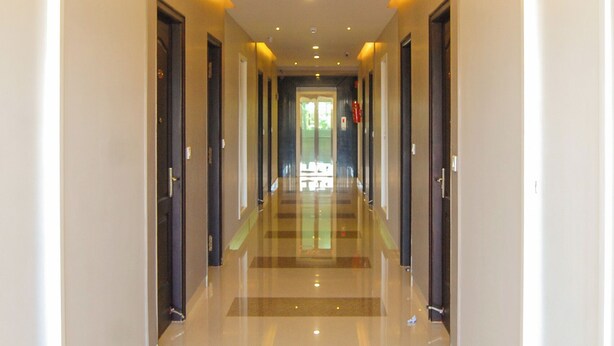 A long, well-lit hallway with doors on both sides, leading to a bright room at the end. - Philomena Hotel & Apartment (Thanjavur)