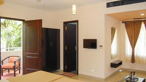 A hotel room with a bed, a chair, a TV, a window with curtains, and a ceiling fan. - Philomena Hotel & Apartment (Thanjavur)