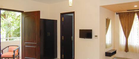 Una habitación de hotel con una cama, una silla, un televisor, una ventana con cortinas y un ventilador de techo.