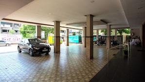 A spacious indoor area with tiled flooring and large pillars, featuring a parked car and a motorcycle. - Philomena Hotel & Apartment (Thanjavur)