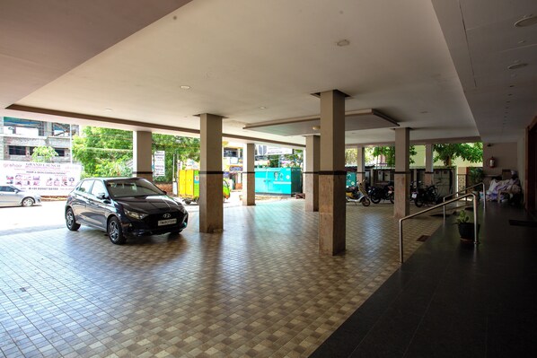 A spacious indoor area with tiled flooring and large pillars, featuring a parked car and a motorcycle.