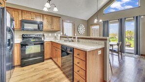 A kitchen with wooden cabinets, stainless steel appliances, a clock, and a view of the outdoors.