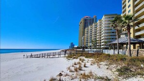 Une plage avec une promenade en bois, de grands immeubles et un ciel bleu dégagé.