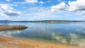 A calm lake with clear water, a rocky shoreline, and distant hills under a partly cloudy sky. - Studio+free parking, 100m to sea (Crikvenica)