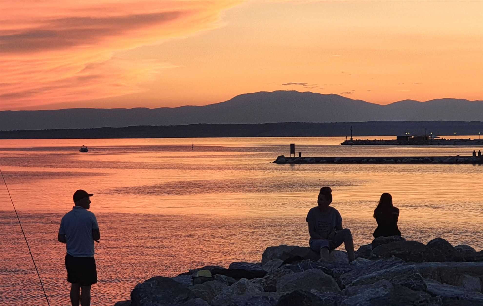 A sunset view over a calm body of water with rocky shores and distant mountains.