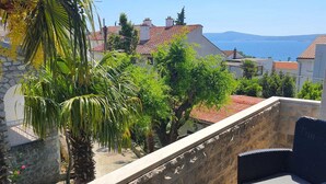 A terrace with stone walls, outdoor furniture, and a view of the sea and buildings. - Studio+free parking, 100m to sea (Crikvenica)