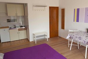 A compact room with a kitchenette, a wooden door, a small white table, and a purple rug. - Studio+free parking, 100m to sea (Crikvenica)