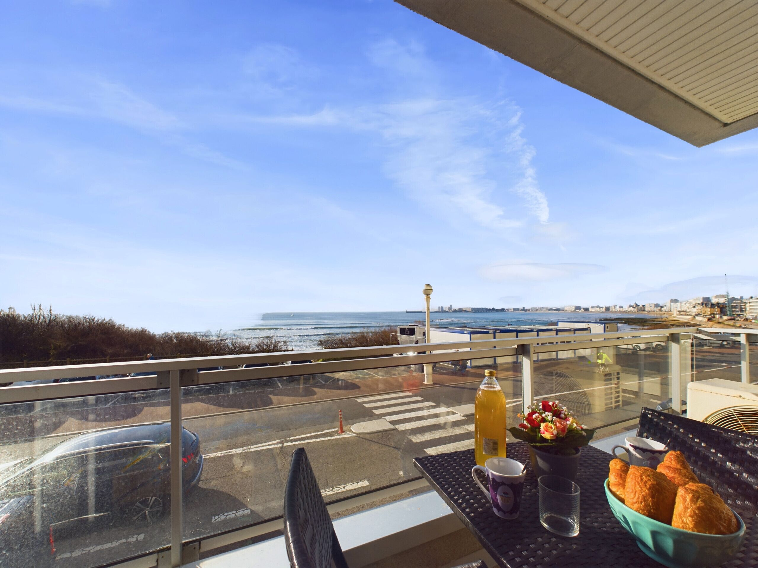 A balcony with a table set for breakfast, overlooking a coastal view.