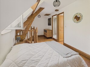 Een slaapkamer met een groot bed, een houten trap, een bureau, een dressoir en een spiegel aan de muur.
