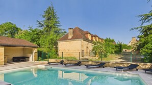 A swimming pool with lounge chairs, a stone building, and surrounding greenery.