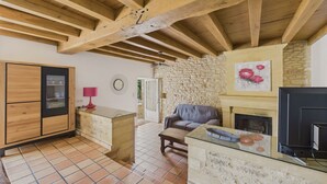 A rustic living room with exposed wooden beams, a stone wall, a fireplace, and a television.