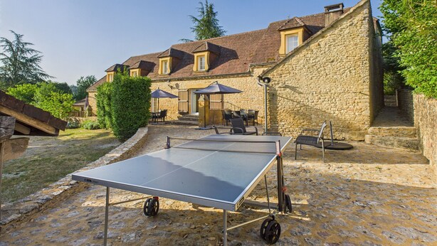 An outdoor ping pong table set up in a courtyard with stone walls and a building in the background.