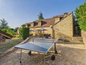 An outdoor ping pong table set up in a courtyard with stone walls and a building in the background.