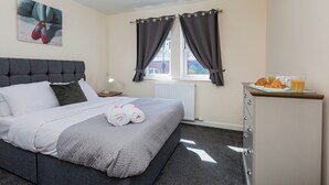 Ein Hotelzimmer mit Bett, Nachttisch, Fenster mit Vorhängen, Heizkörper und einer Frühstückstheke mit Croissants und Saft.
