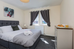 Une chambre d’hôtel avec un lit, une table de chevet, une fenêtre avec des rideaux, un radiateur et un buffet pour le petit-déjeuner avec des croissants et du jus de fruits.
