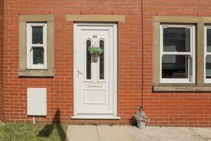 A red brick building with a white door marked '66', a small window above the door, and a utility box to the left.
