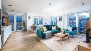 En rummelig opholdsstue med en grøn sofa, et træbord og udsigt til byen gennem store vinduer.