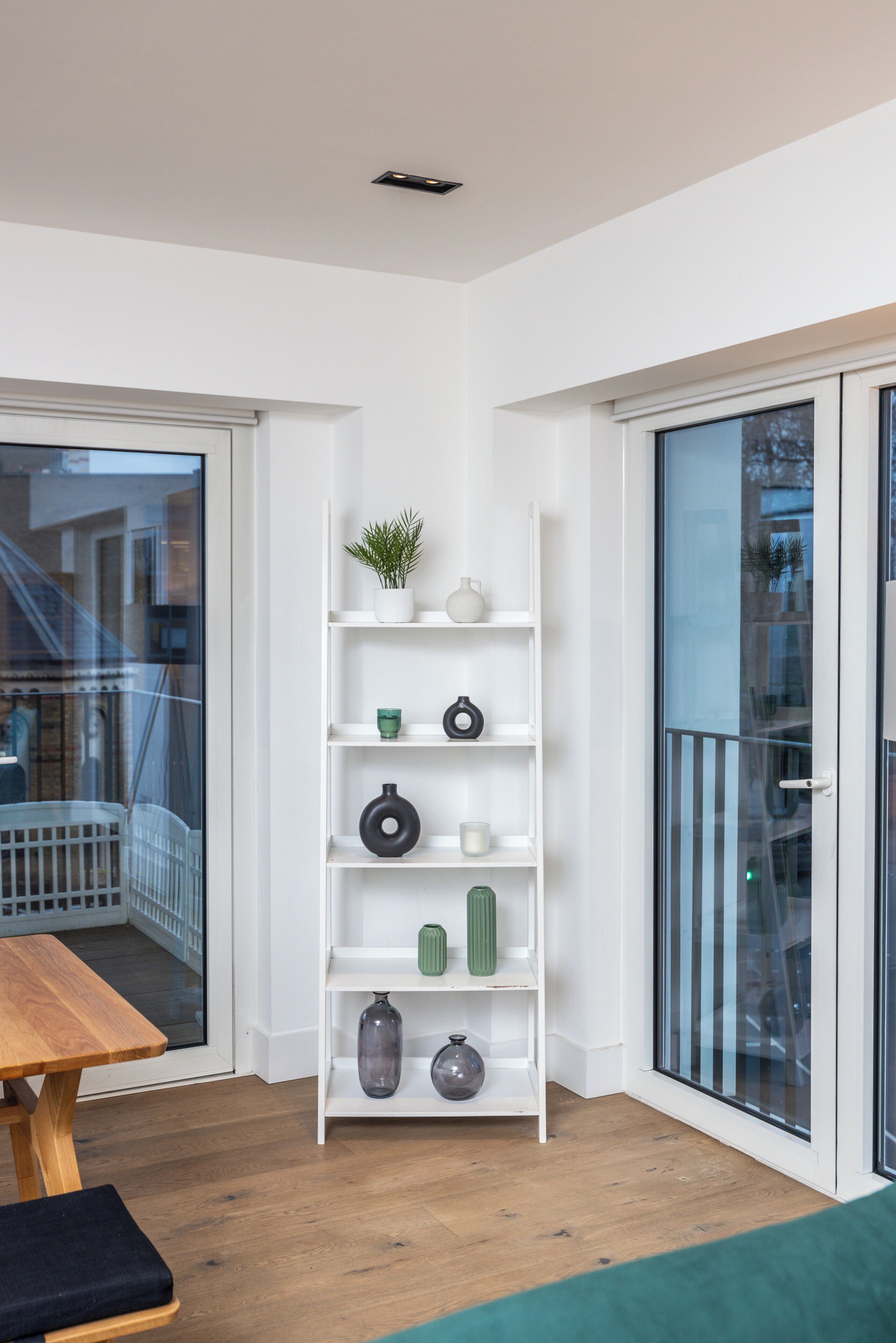 A modern room with a white bookshelf, wooden flooring, and a glass door leading outside.