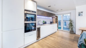 Et moderne køkken med indbyggede ovne, en vask og et stort vindue med udsigt til en balkon.