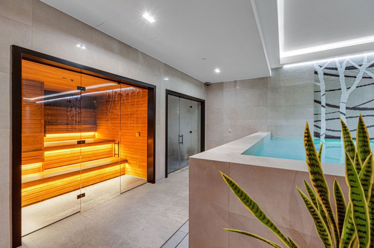 A modern spa area with a heated floor, a glass door entrance, and a pool area with a geometric wall design.