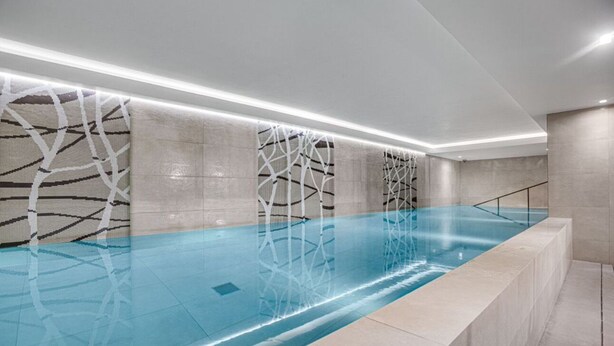 En moderne indendørs swimmingpool med et geometrisk vægdesign og en klar blå vandoverflade.