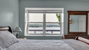 Quarto com cama, mesa de cabeceira, luminária, janela com vista para um corpo d'água e espelho.