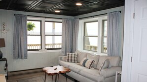Um quarto aconchegante com sofá, mesa de centro de madeira e janelas grandes com cortinas.