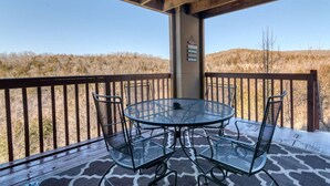 A covered outdoor patio with a round table and four chairs, overlooking a hilly landscape. - Condo next door to SDC (Branson)