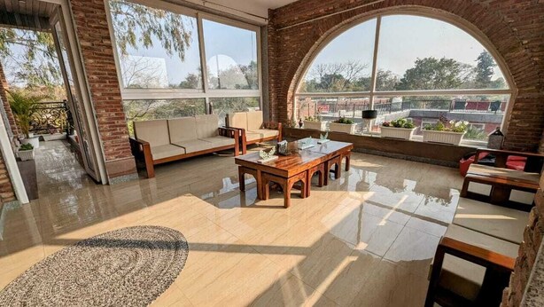 A spacious balcony with a wooden table and chairs, a sofa, and potted plants. - Ayaansh Resort (Sohna)