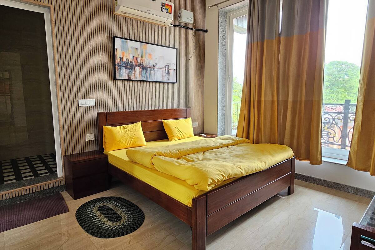 A bedroom with a wooden bed, yellow bedding, a window with curtains, a door, and a wall-mounted air conditioner.
