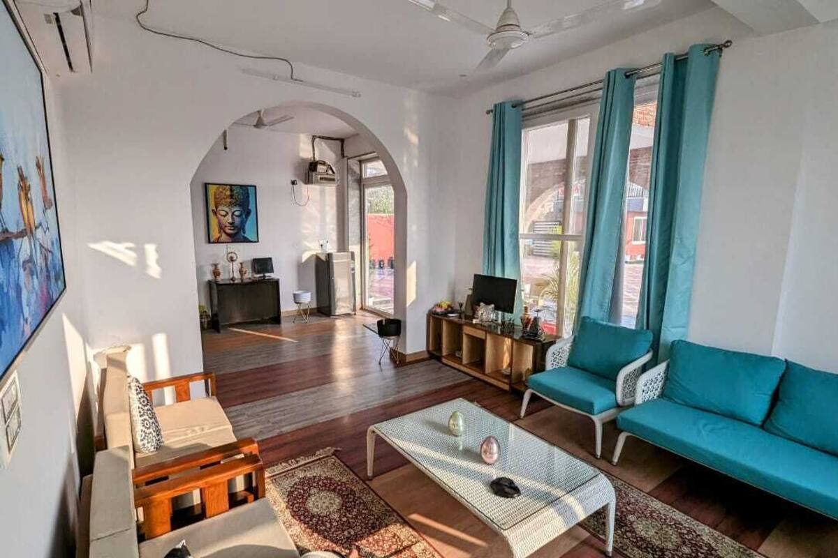 A spacious living area with a blue sofa, wooden coffee table, and a TV. There is a painting on the wall and a window with curtains.