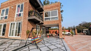 A two-story brick building with large windows, a balcony, and a covered outdoor seating area. - Ayaansh Resort (Sohna)