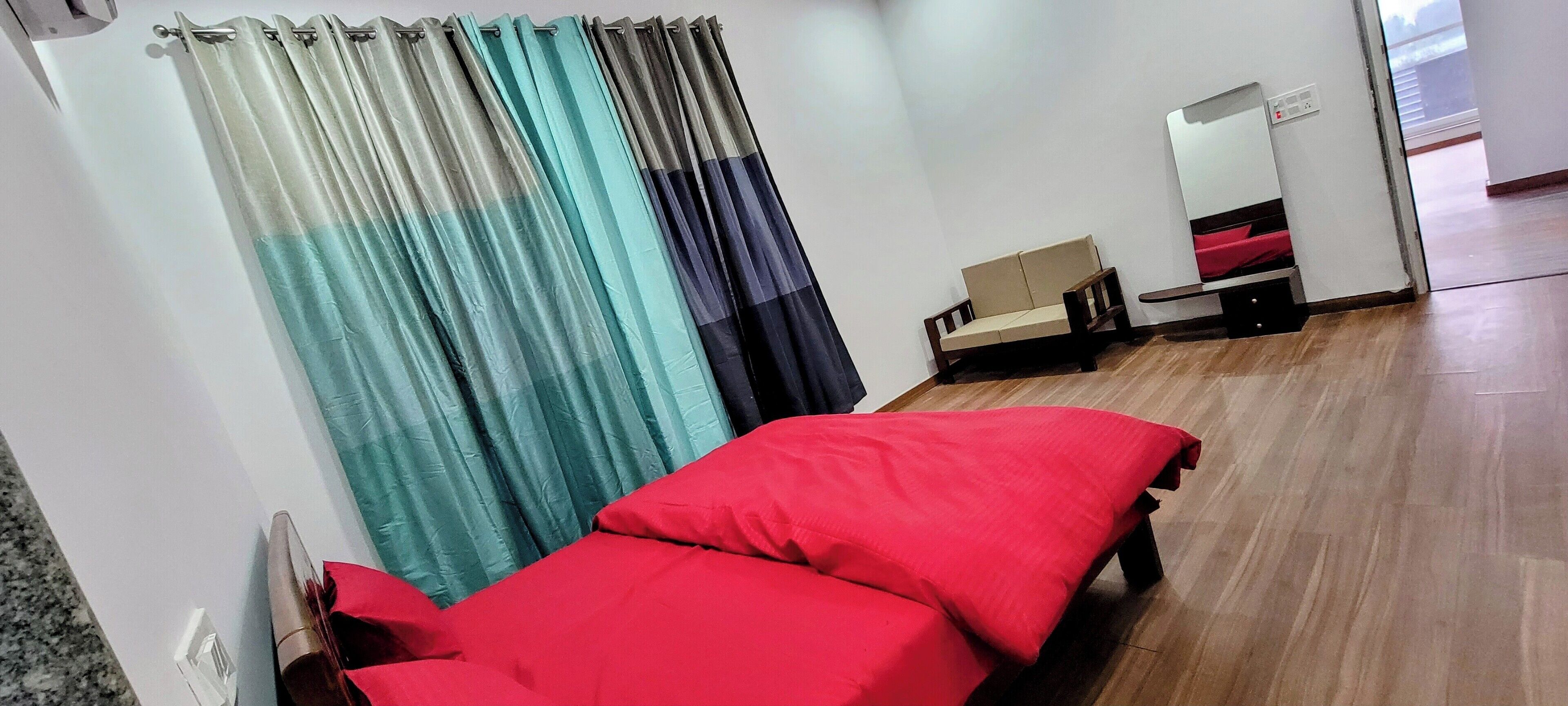 A room with a bed, a small sofa, a mirror, and a window with curtains.