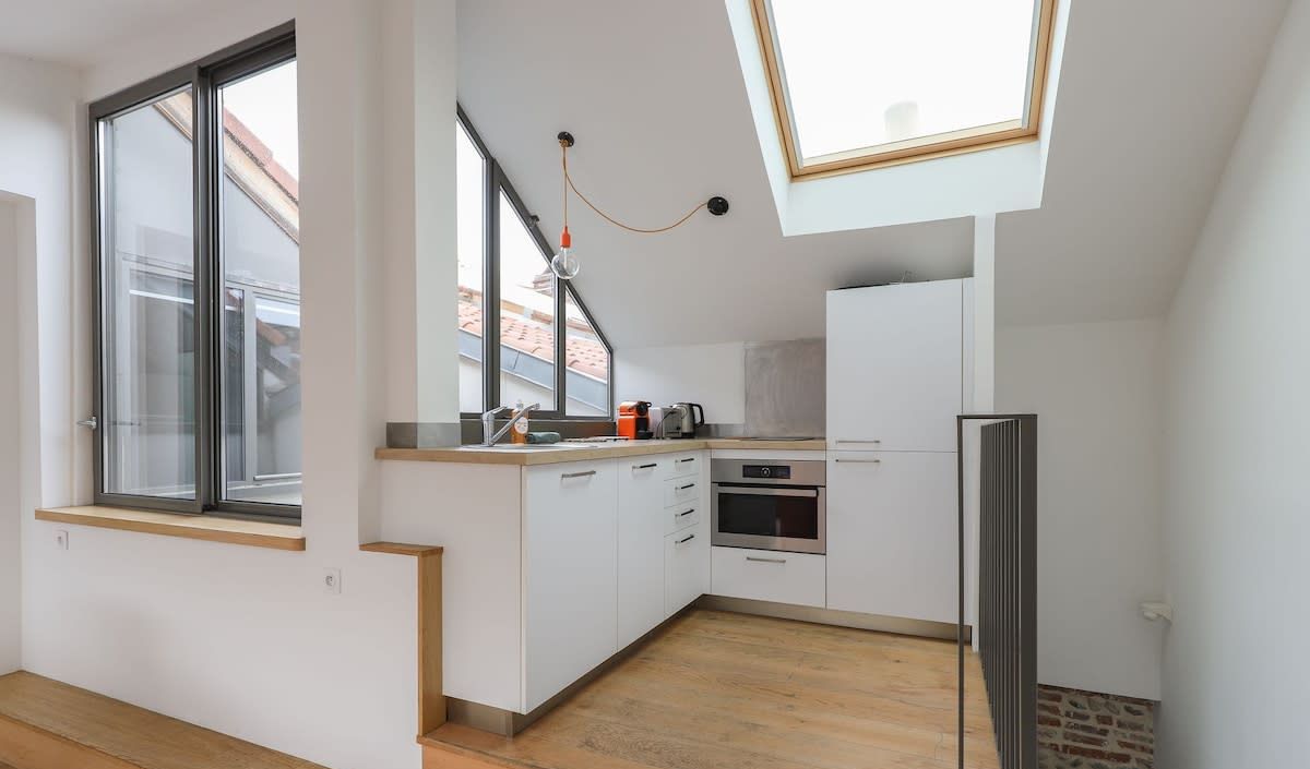 Une cuisine moderne avec des meubles blancs, un four encastré et une lucarne.