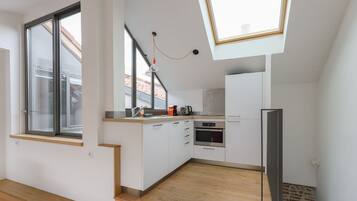 Une cuisine moderne avec des meubles blancs, un four encastré et une lucarne.