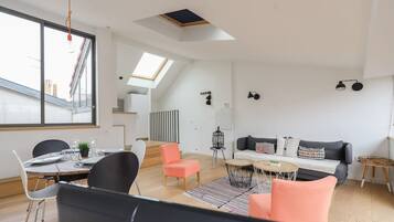 A modern living space with a dining area, a sofa set, a small table, and a staircase leading to an upper level.