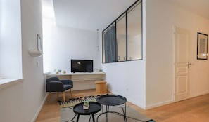 Ein modernes Wohnzimmer mit Fernseher, zwei schwarzen Sessel, einem kleinen Tisch und einem großen Fenster.
