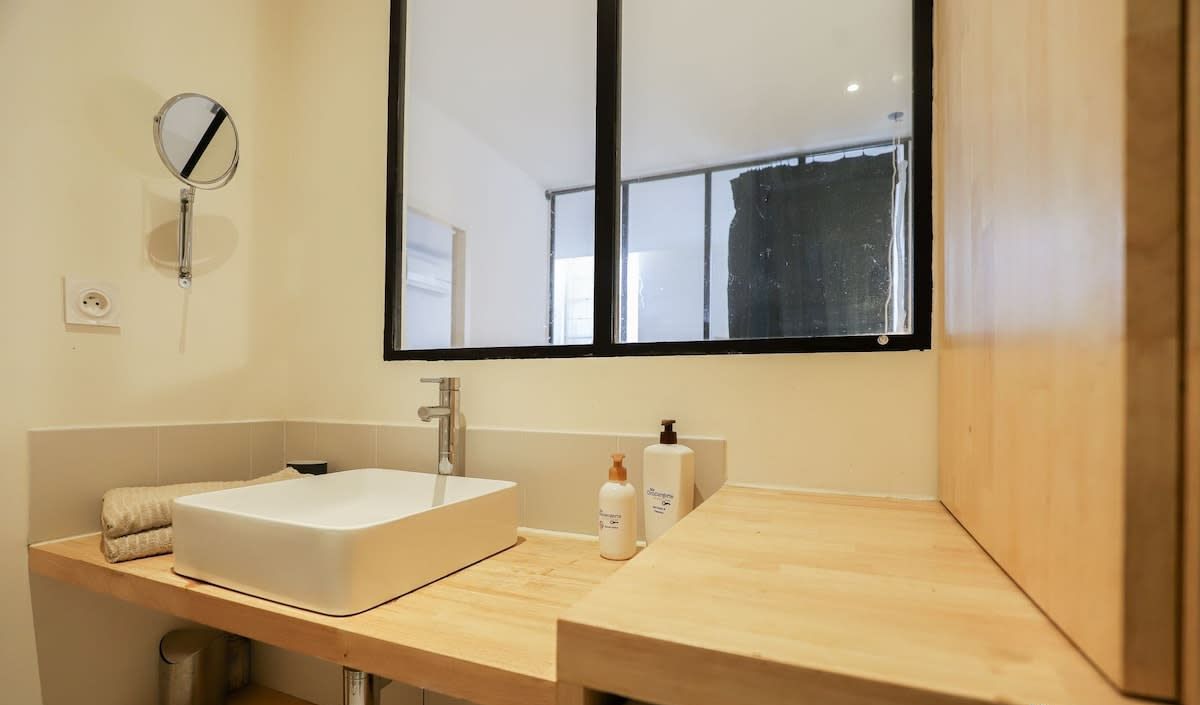 Un baño moderno con un espejo grande, un lavamanos blanco y encimeras de madera.