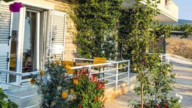Un edificio con un balcone, immerso nel verde e circondato da piante fiorite.