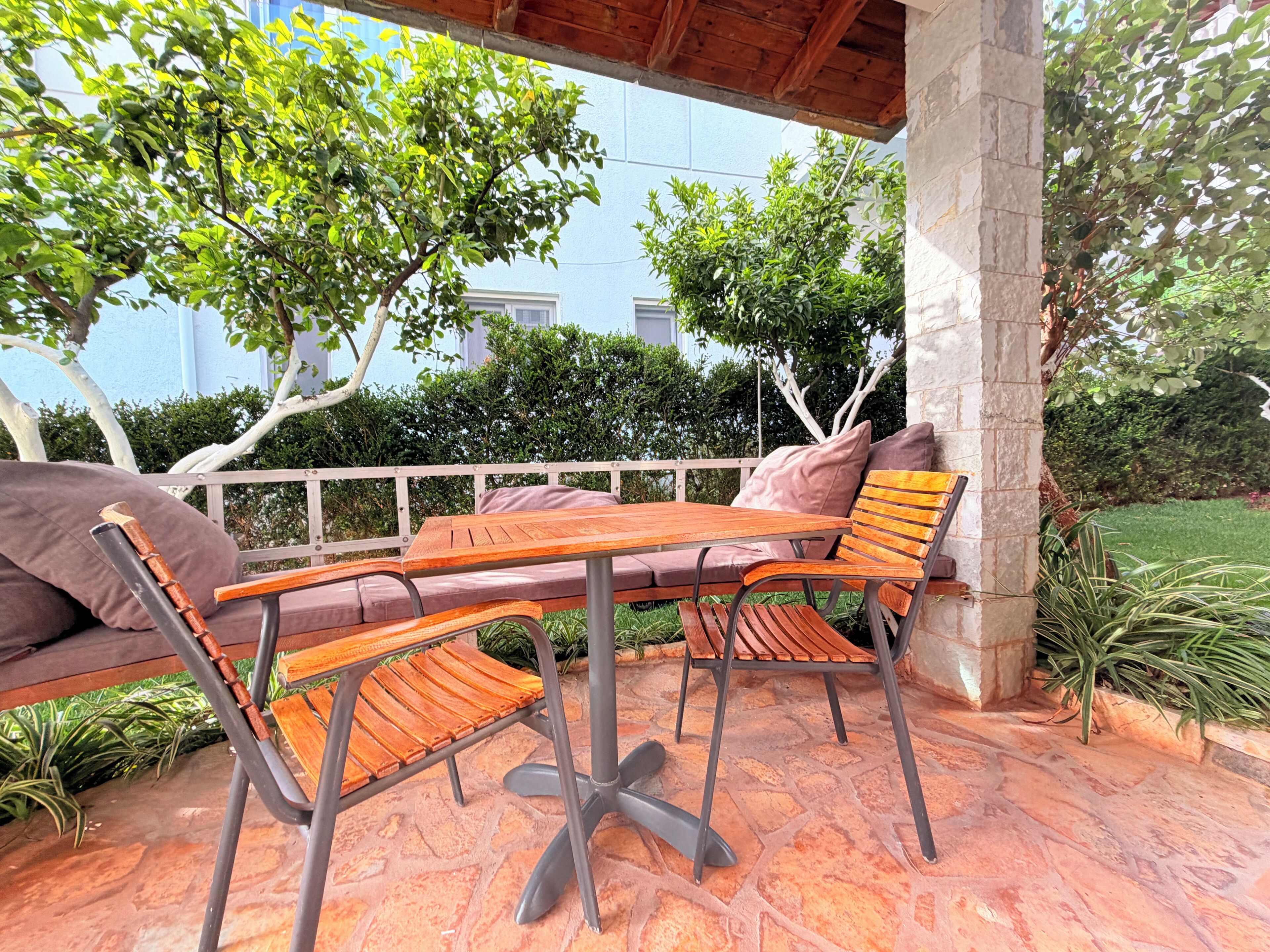 Un patio al aire libre con una mesa y sillas de madera, un banco acolchado y piso de piedra.