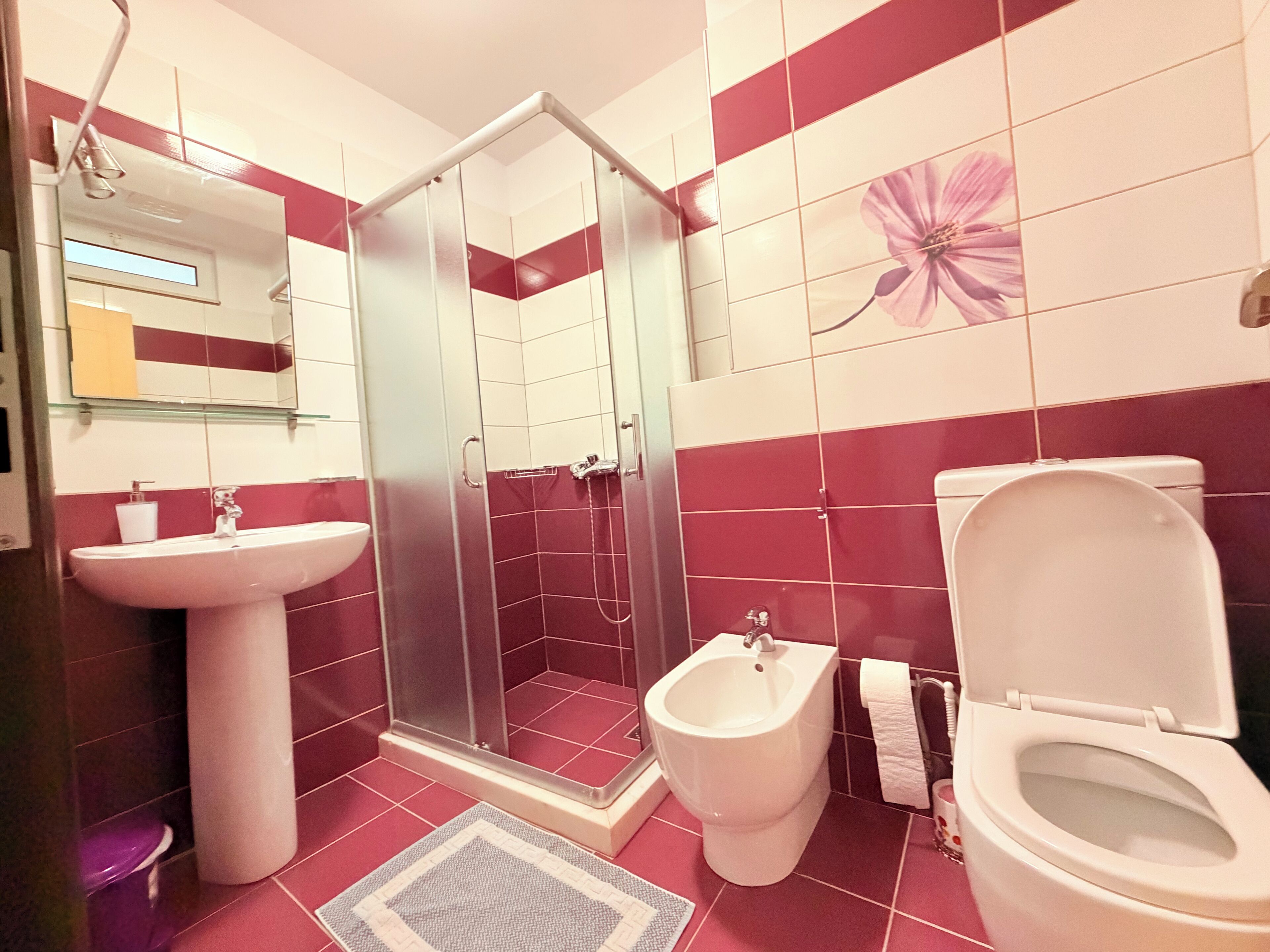 A bathroom with a glass-enclosed shower, a pedestal sink, a bidet, and a toilet.