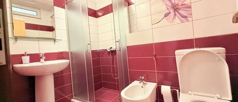 A bathroom with a glass-enclosed shower, a pedestal sink, a bidet, and a toilet.
