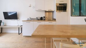 A modern kitchen with white cabinets, a wooden dining table, and a built-in oven.
